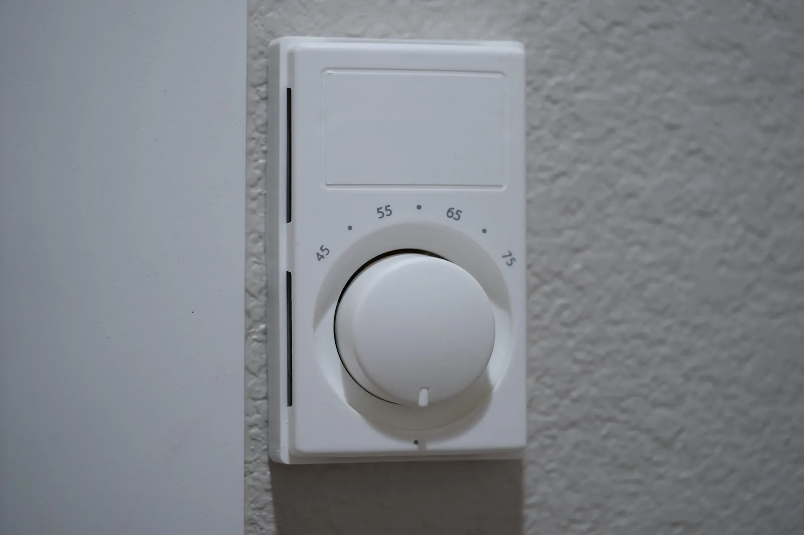 White manual dial thermostat with a 45 to 75 degree scale mounted on a textured wall