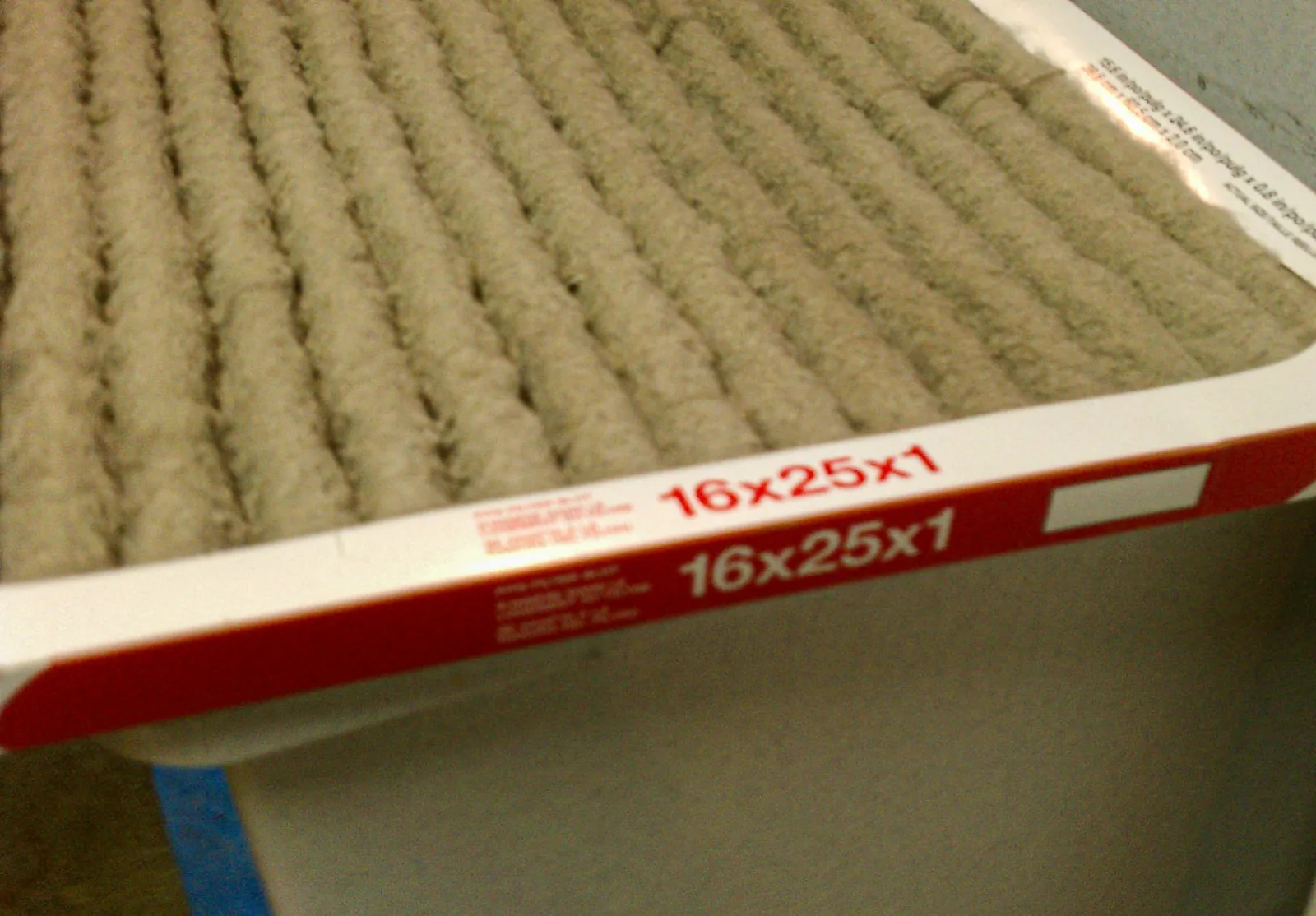Used 16x25x1 pleated furnace air filter, its pleats coated in gray-brown dust